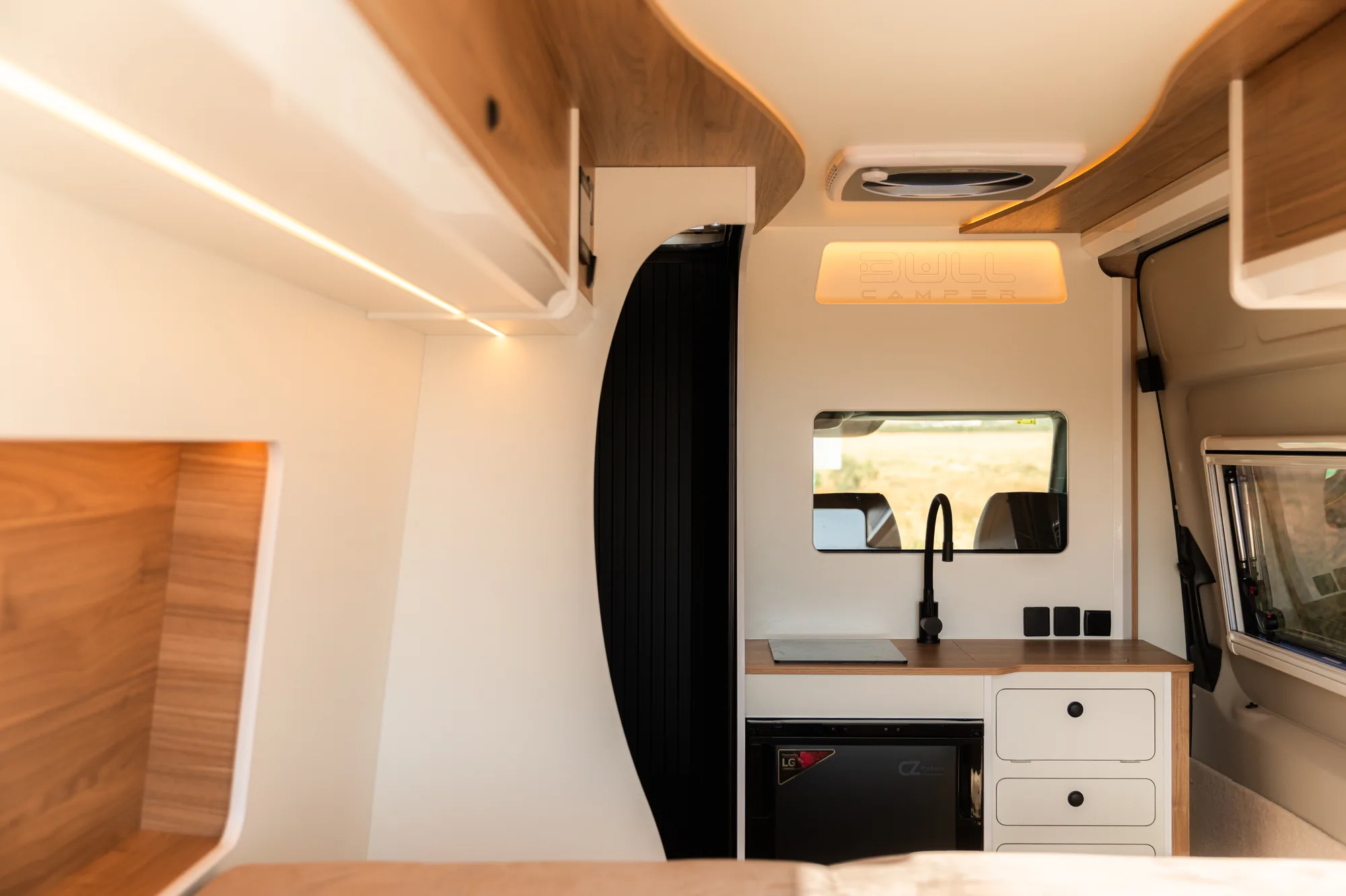 Interior en blanco y madera de la Volkswagen Crafter con cocina, armarios altos curvos y ventanas