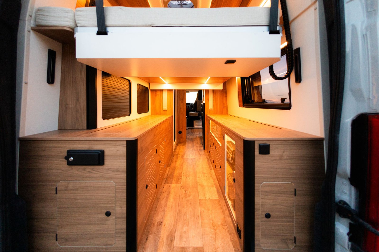 Vista desde las puertas traseras: cama elevable sobre armarios de madera a ambos lados del pasillo