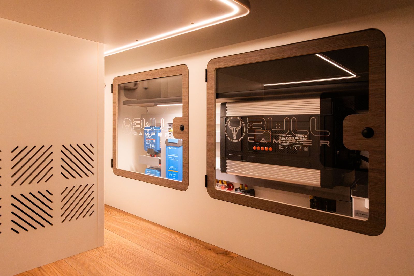 Cuadro eléctrico con cargadores Victron e inversor tras ventanas con el logo Bullcamper grabado